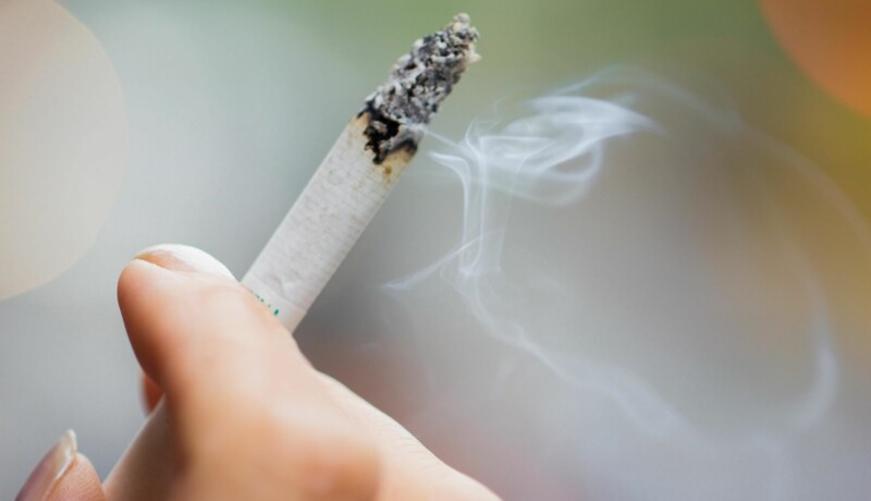 En hand som håller i en rykande cigarett.