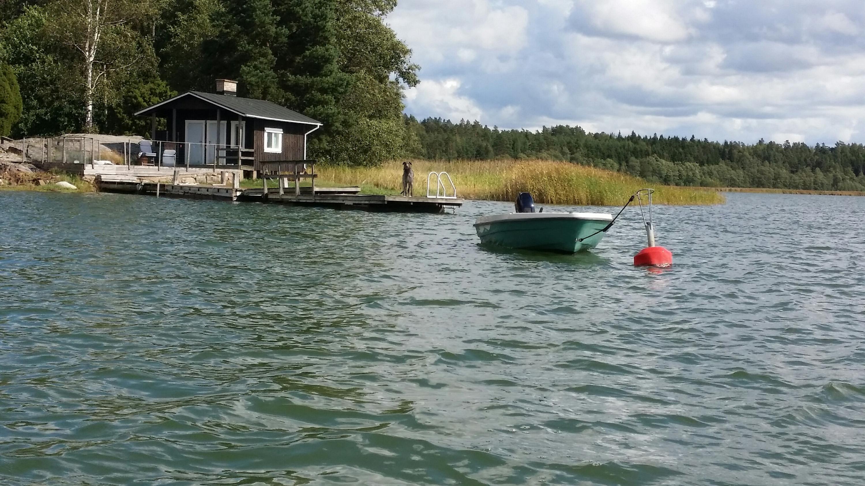 Liten stuga vid vattnet. En liten båt i förgrunden.