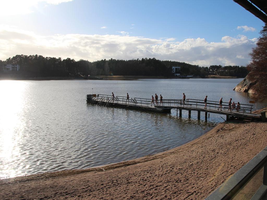 sandstrand med brygga där många går mot vattnet