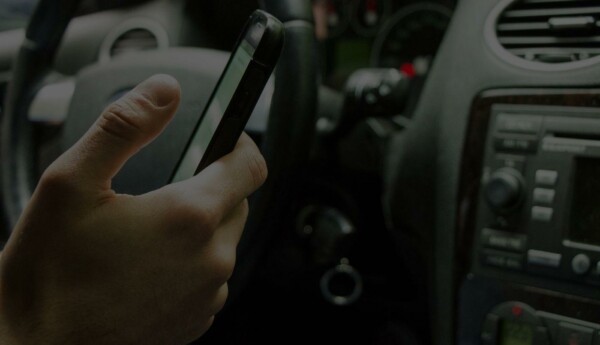 Hand som håller i mobiltelefon i förarsätet på en bil.
