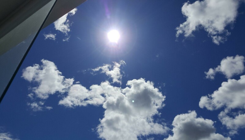 Sol på en blå himmel med några små moln.