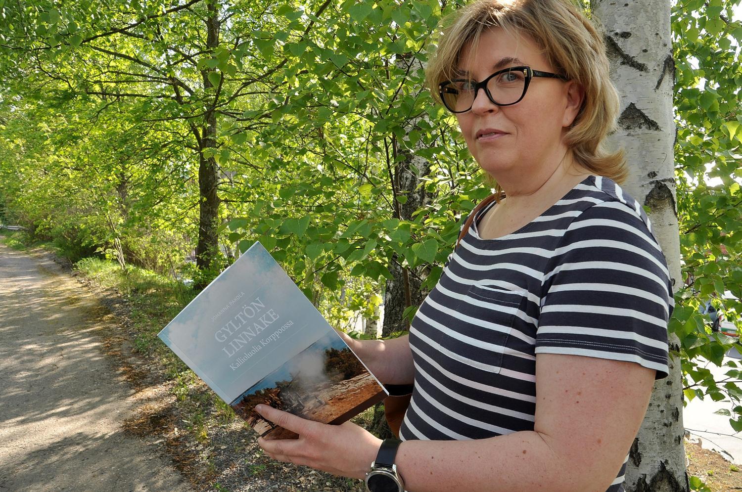 Kvinna med bok i handen , i bakgrunden grönskande träd