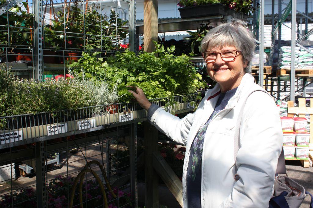 Kate Lindgren med vit jacka ler in i kameran, planteringsväxter i bakgrunden.