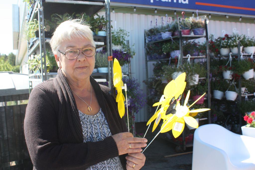 Kerstin Vuorio håller i några gula plastblommor, ställningar med blommor i bakgrunden.
