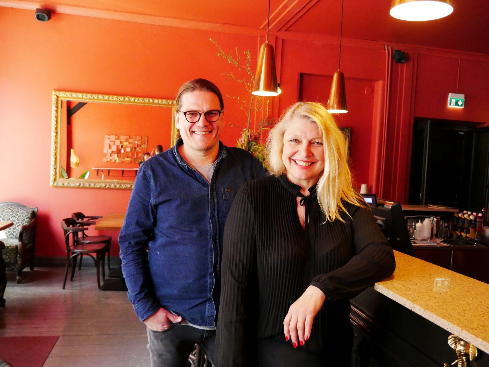 Två personer står vid bardisken i en bar med röda väggar
