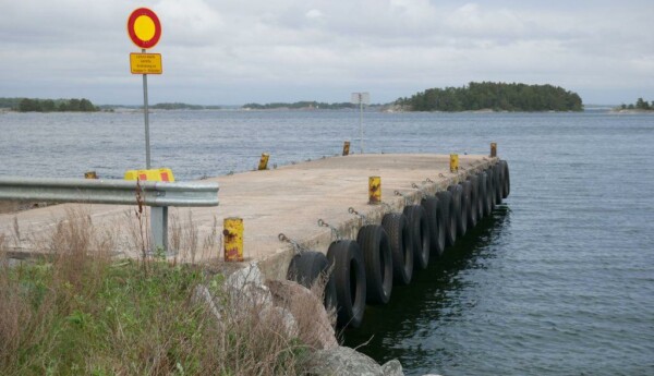 Vikare bryggan i Hitis, trafikmärke på bryggan, vatten, grå himmel och holme i bakgrunden