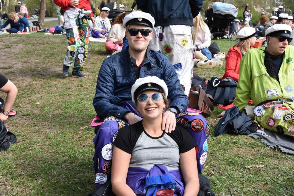 Två unga personer sitter i en park iklädda studentmössor.
