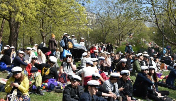 Människor på picknick i en solig och grön park. Många har på sig studentmössor.