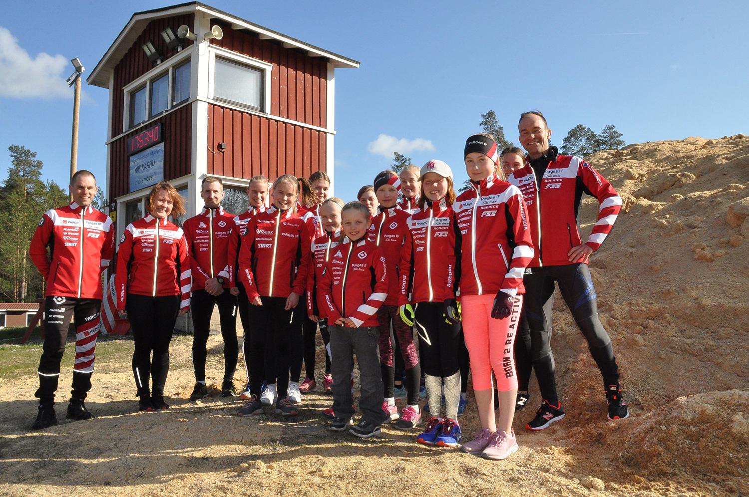 Ett gäng skidjuniorer och tränare uppställda framför en spåntäckt hög med konstsnö