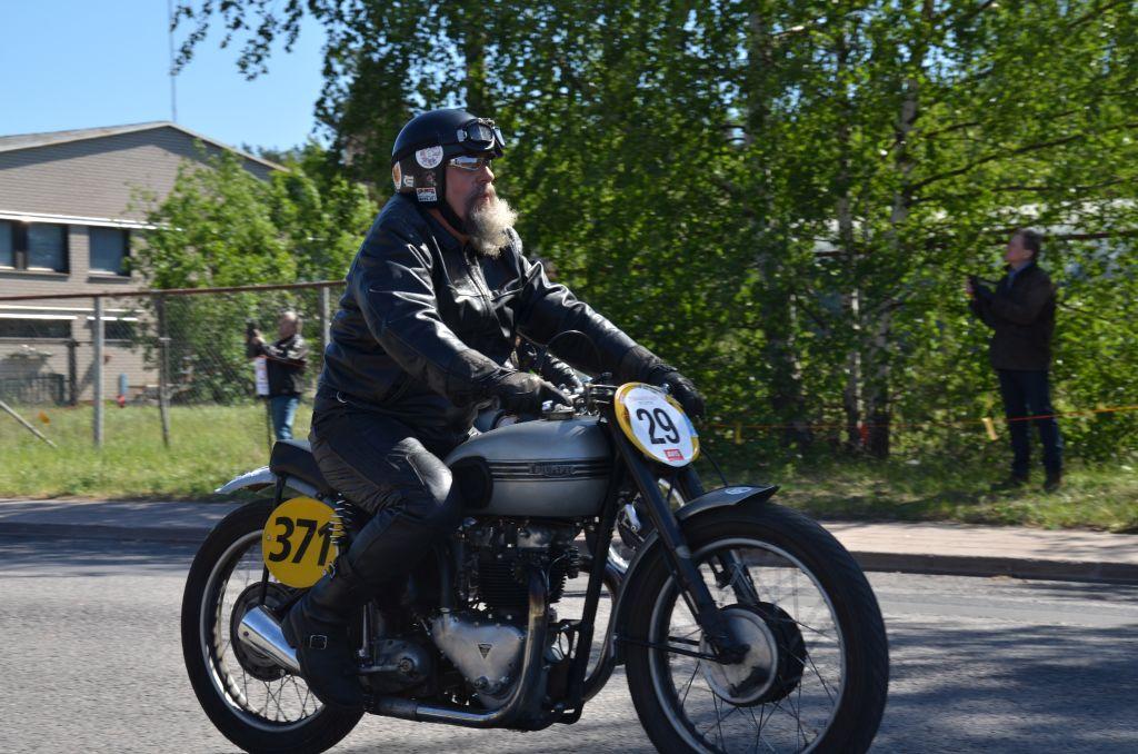 En skäggig man åker på en gammal Triumph motorcykel.