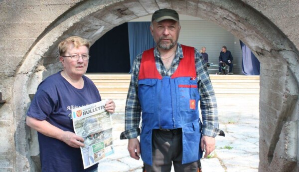 Runa Heino håller i Västanfjärds Bulletin och står bredvid Max Andersson, under en ruinport i sten.