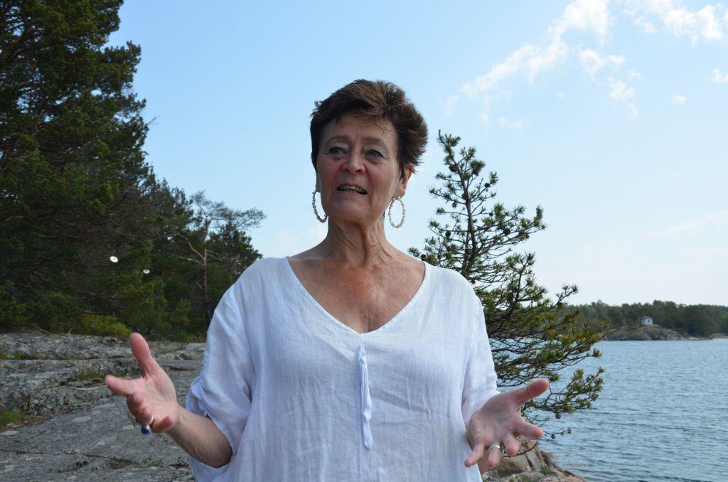 En kvinna klädd i vitt står och gestikulerar på ett berg. I bakgrunden syns havet.