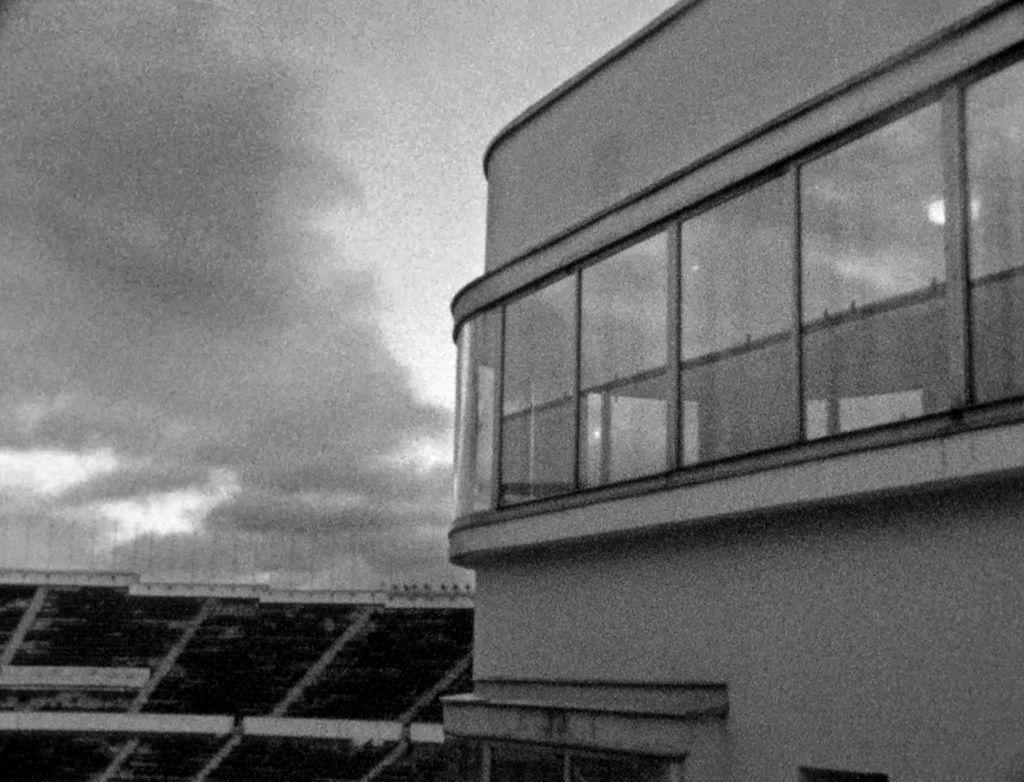 Svartvit bild av en del av Helsingfors Olympiastadion mot en mulen himmel.