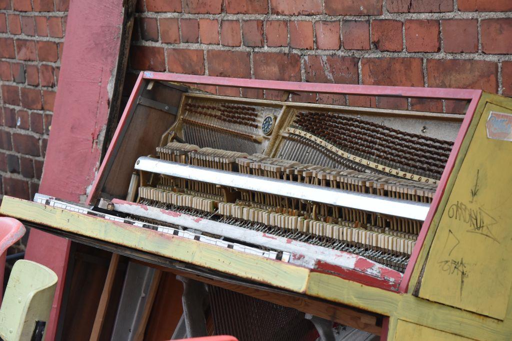 Ett totalförstört piano står lutat mot en tegelvägg