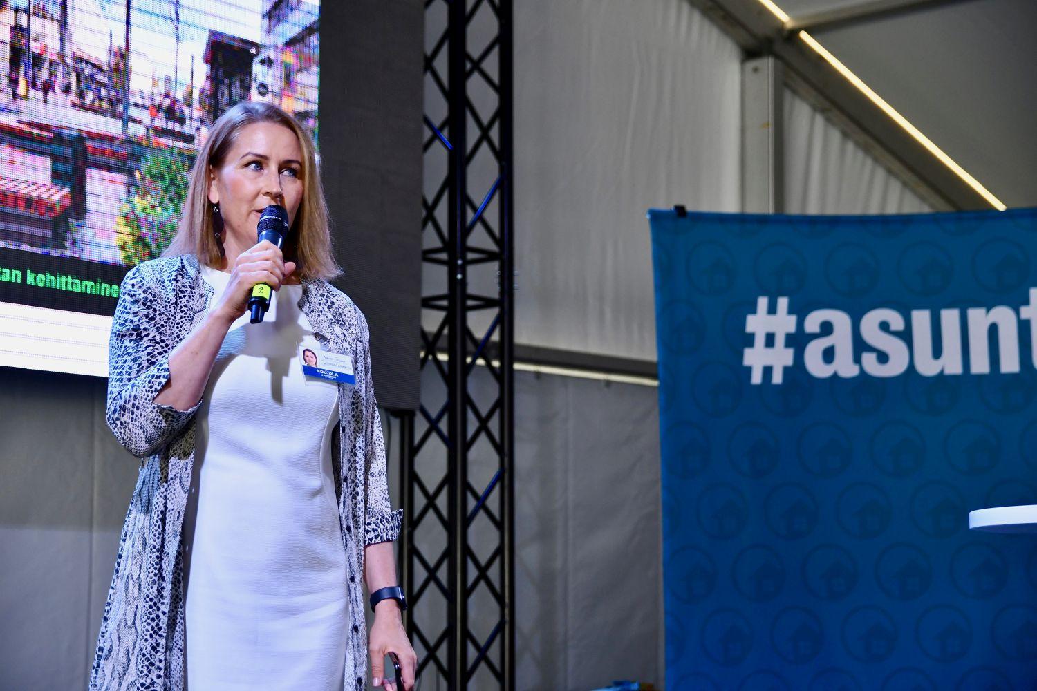 Marita Toikka talar i mikrofon på scen.