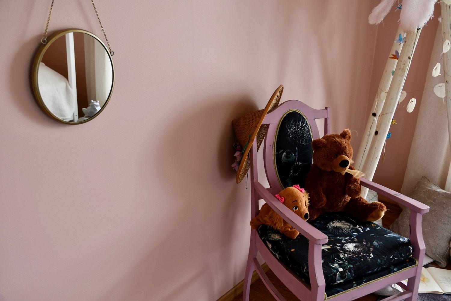 Ett rosa barnrum med en spegel på väggen och en stol där en nallebjörn sitter. På stolen hänger också en solhatt.