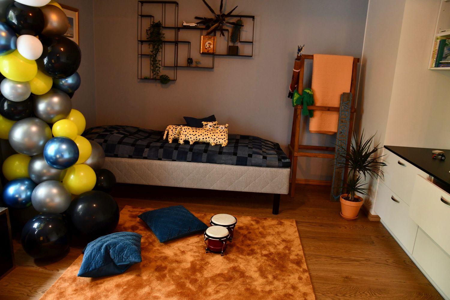 Ett barnrum inrett med bland annat ballonger i gult, grått och svart. Överlag aningen mörkare färger men mysigt i rummet.