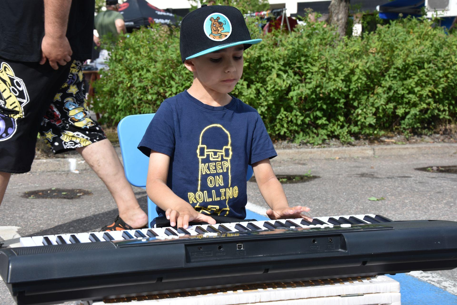 En liten pojke sitter ute på ett torg och spelar på en synt.