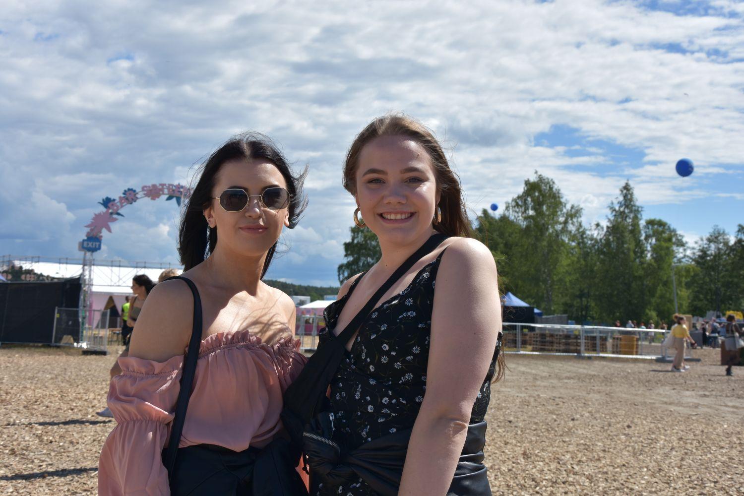 två unga kvinnor håller om varandra på ett festivalområde. Solen lyser.