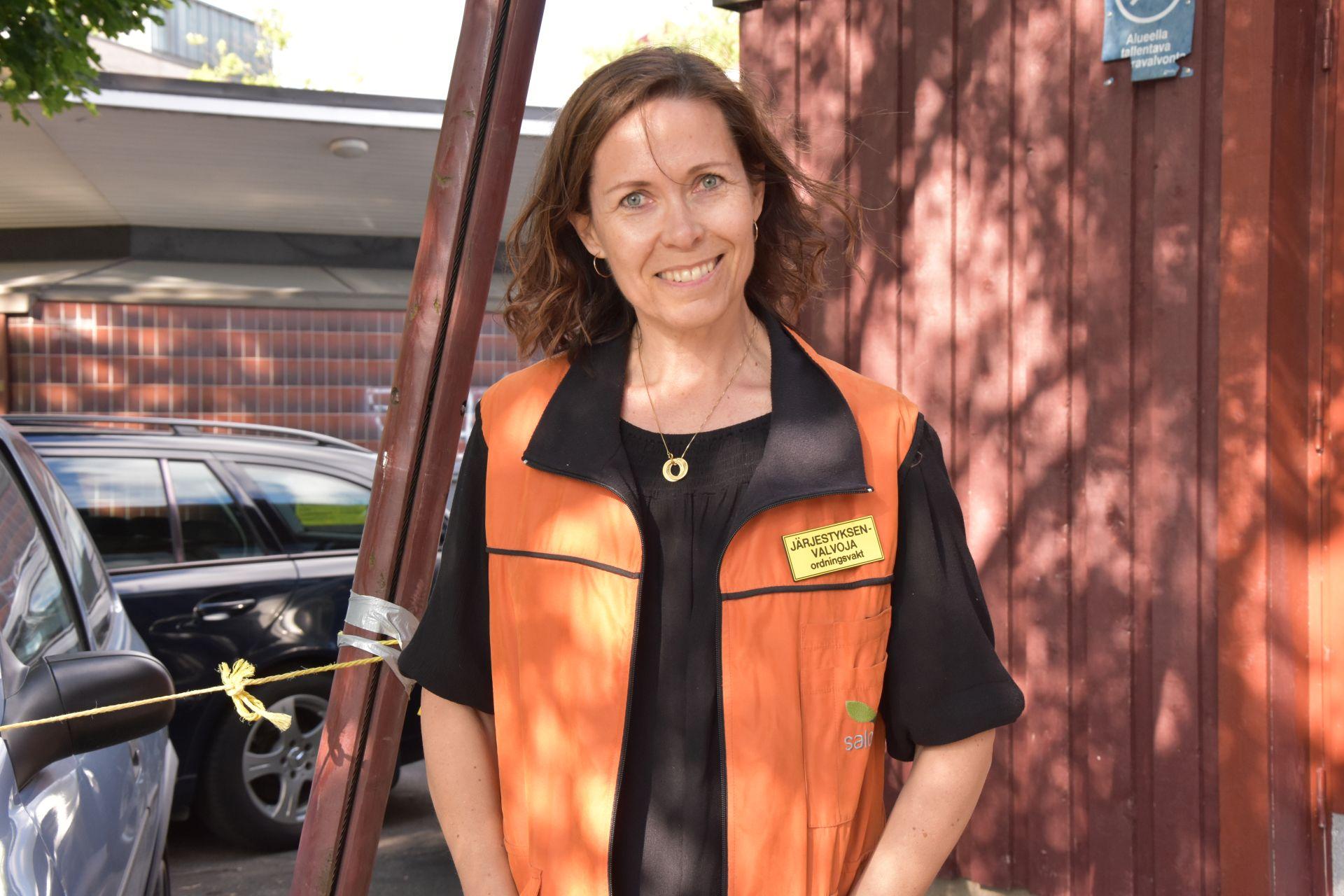 En kvinna i en orange säkerhetsväst lär in i kameran.
