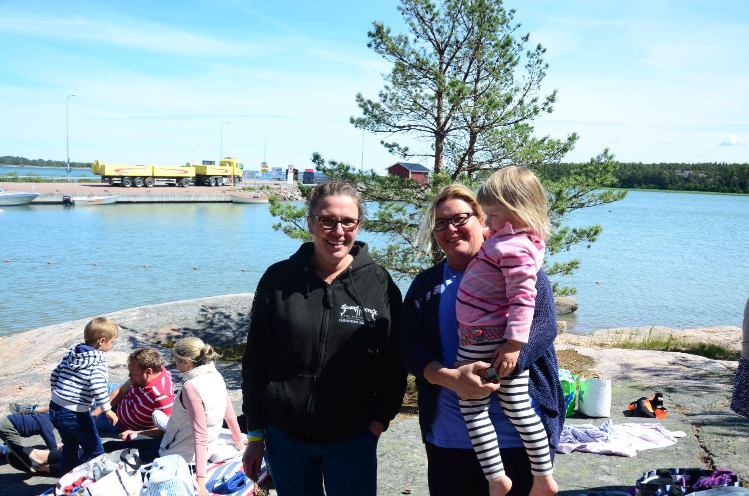 Tove Peltoniemi och Lotta Lindberg-Jaakkola med lilla Kia i famnen står på stranden.