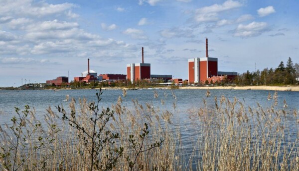 i förgrunden ser man vegetation och vatten. På andra sidan vattnet ser man siluetten av kärnkraftverket