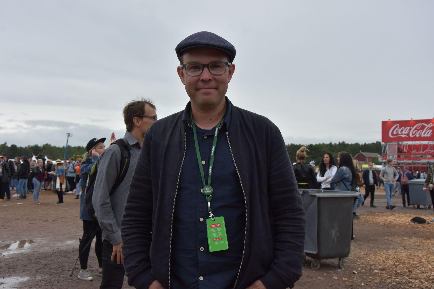 En man står på ett festivalområde i bakgrunden ser man ett hav av människor.