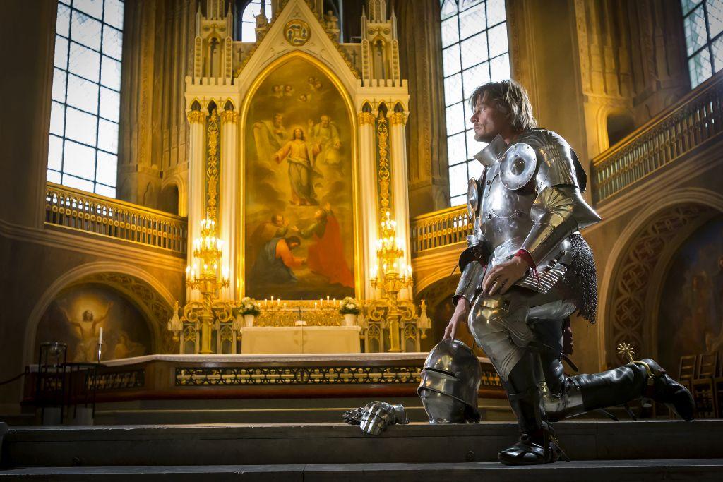 En person klädd i medeltida riddarkläder står knäböjd framför altaret i Åbo domkyrka.
