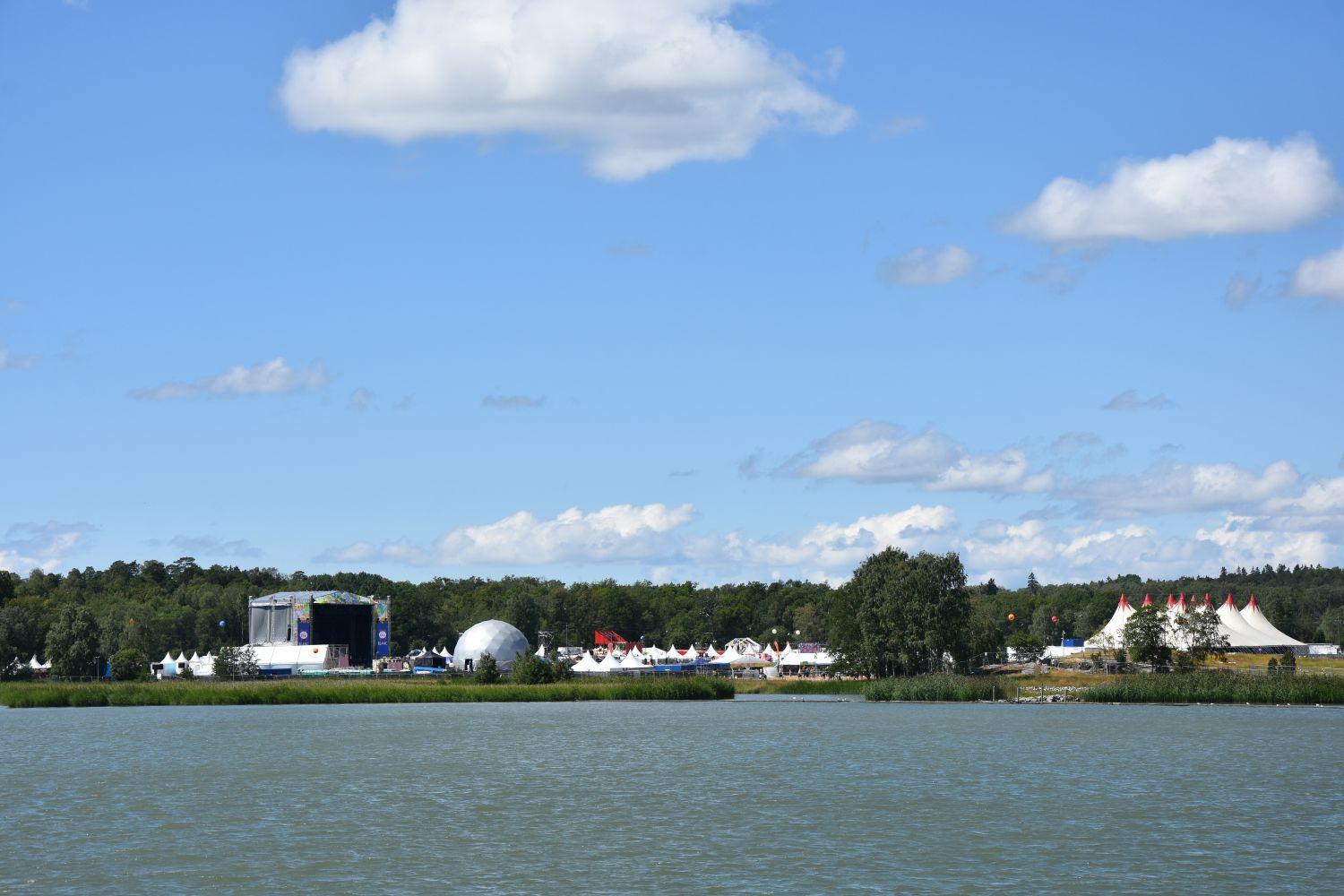 foto över området från vattnet. Man ser scener och byggnader. Solen lyser.