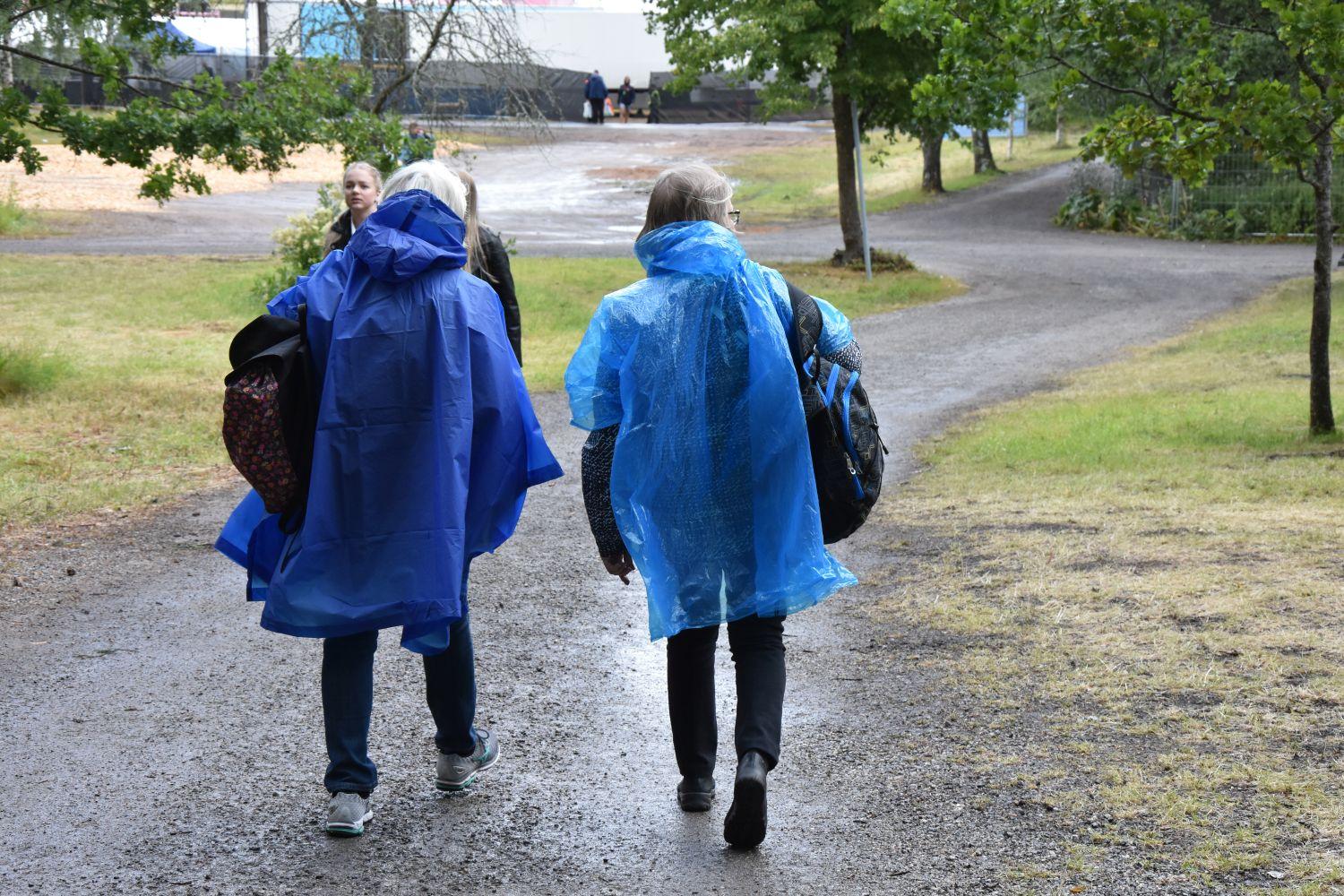 två personer klädda i blåa regnrockar går längs en lerig stig