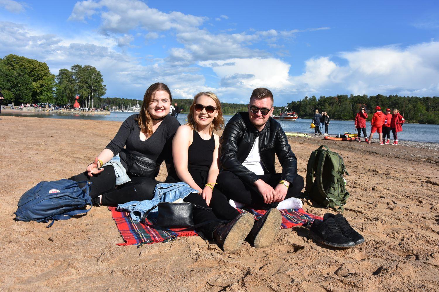 tre personer sitter på en filt på en strand