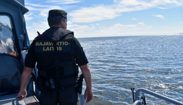 En sjöbevakare står på en båt och tittar ut över havet. På hans rygg står det "Rajavartiolaitos"