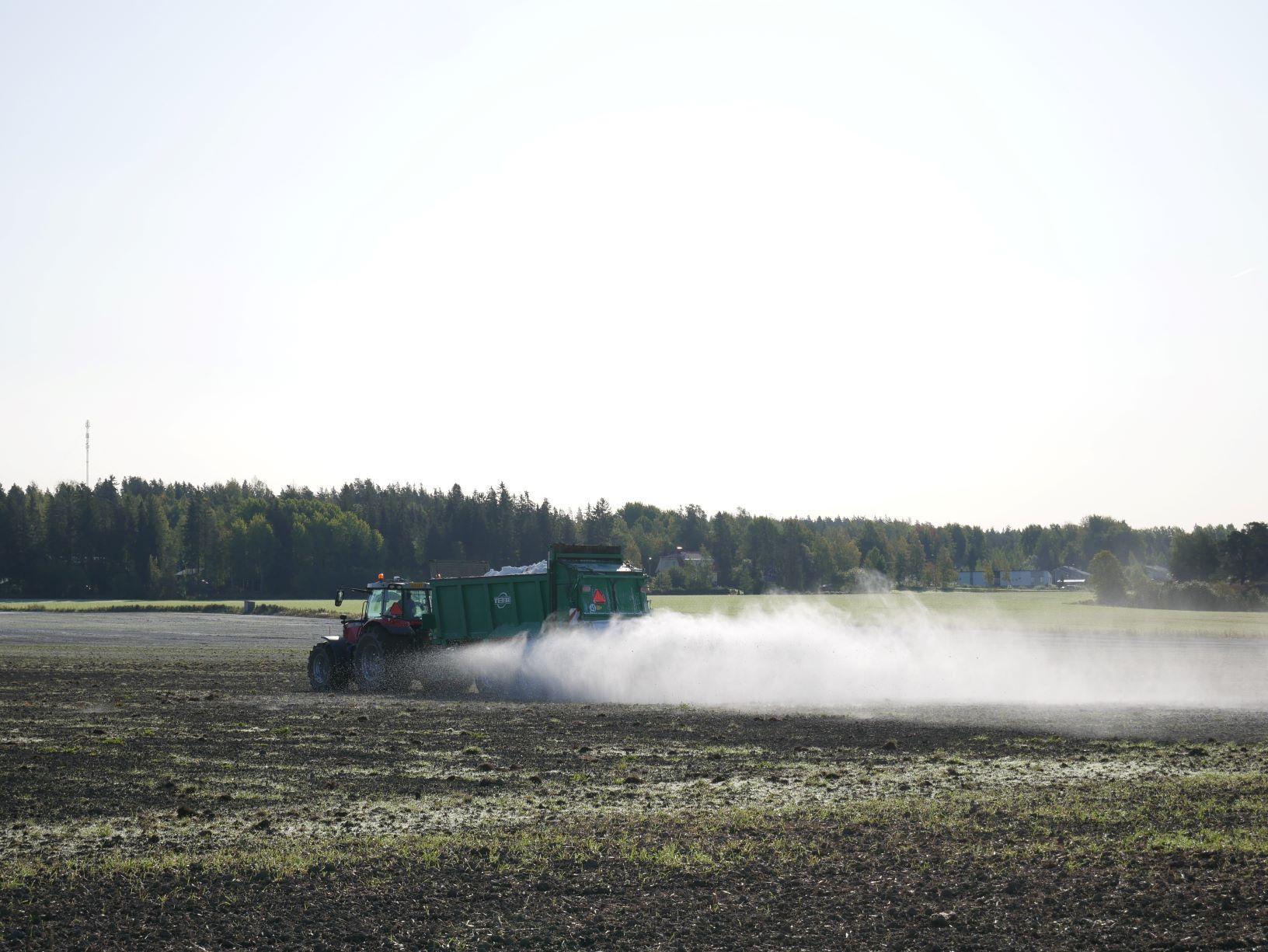 En traktor som sprider ut något på en åker.