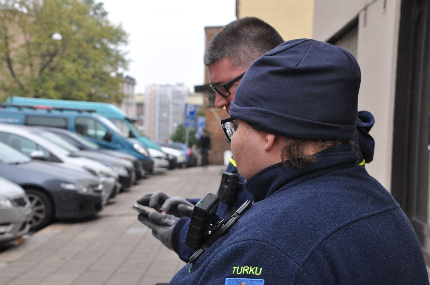 Två parkeringsövervakare granskar en mobil.