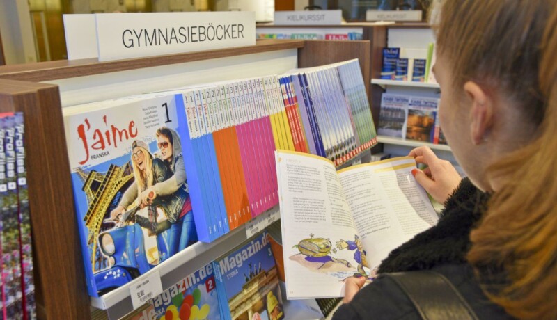 En flicka bläddrar i en bok vid en affärshylla.
