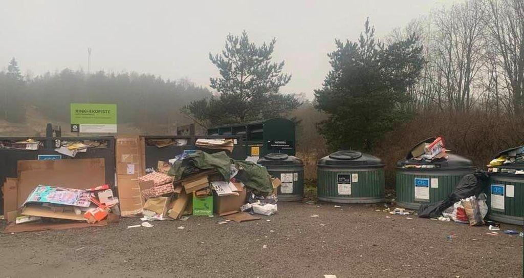 En återvinningspunkt med flera sopkärl. På marken ligger en hög med främst kartongavfall.