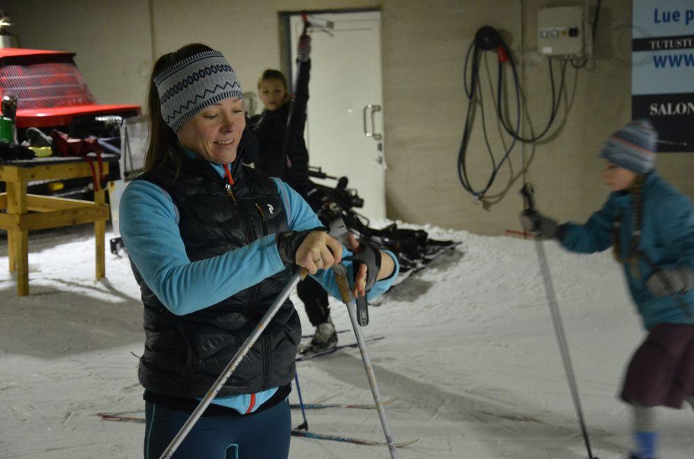 En kvinna klädd i sportiga kläder står i en snötäckt hall och lägger på sig ett par handskar.