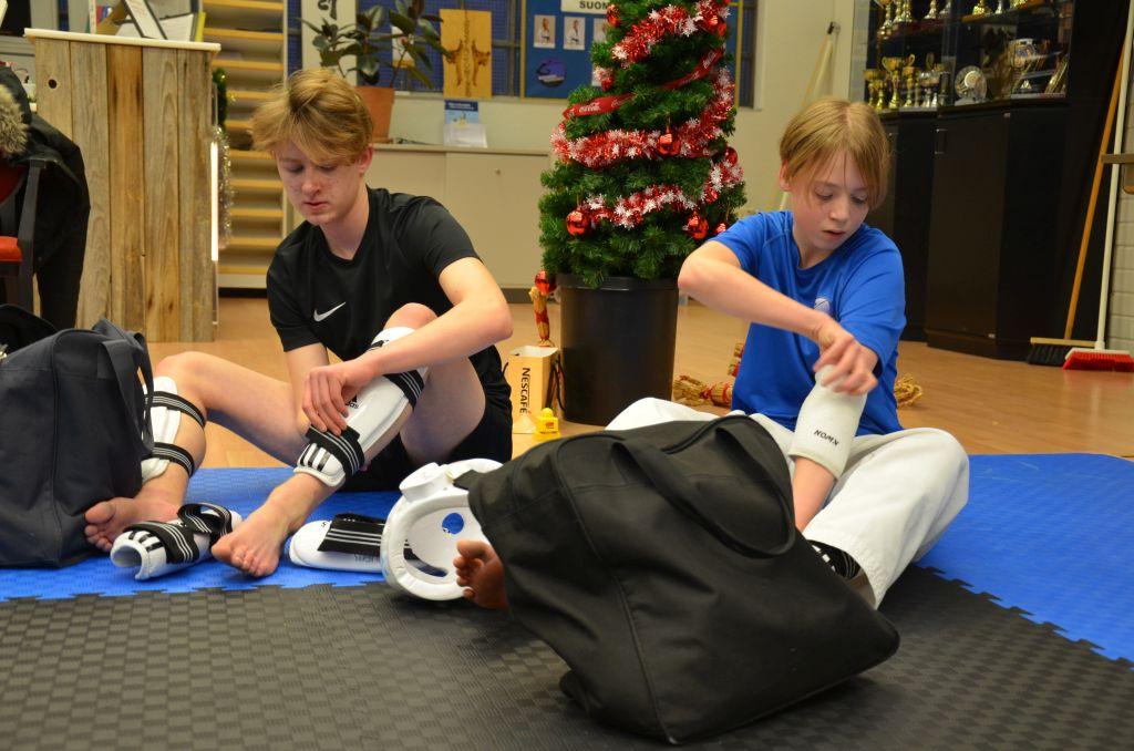 Två pojkar sitter på ett gymgolv och sätter på sig skyddsutrustning.