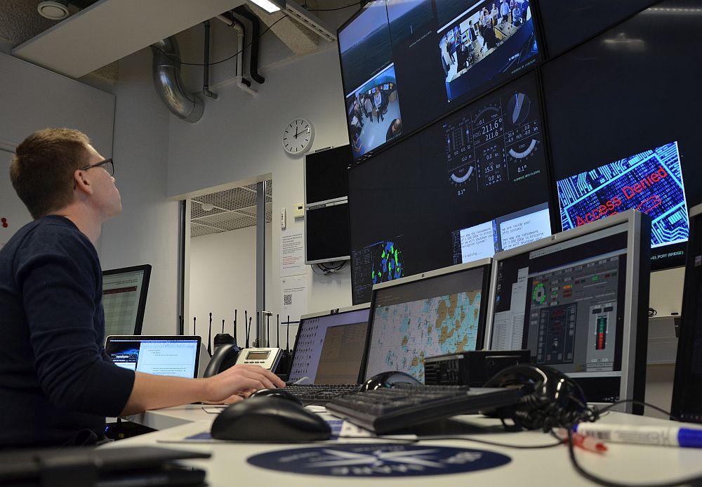Man sitter vid en vägg med stora dator- och teveskärmar