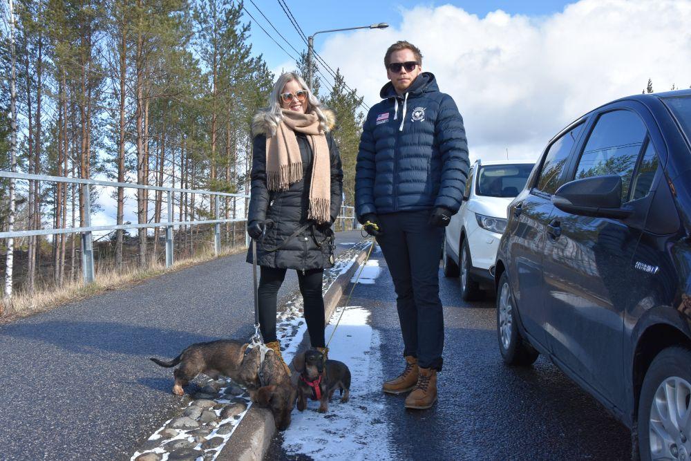 Ung kvinna och man med två taxar står intill en bilkö.