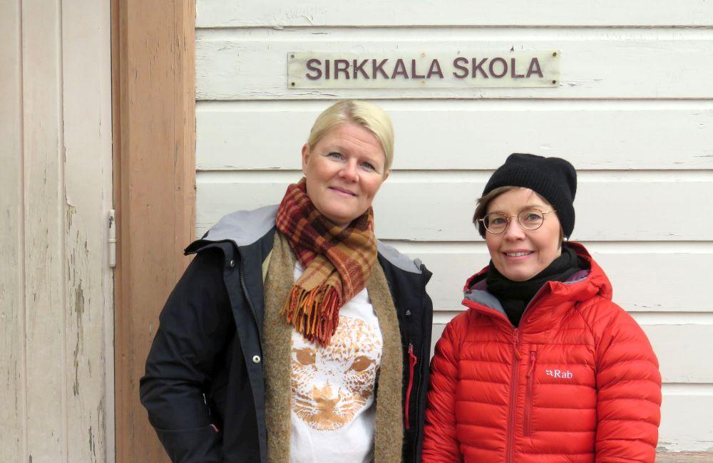 Två kvinnor framför skolas trävägg