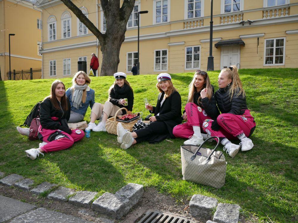 Sex unga kvinnor klädda i studentoveraller har picknick