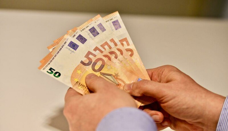 Händer som håller i flera 50 euros sedlar.