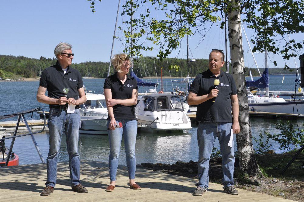 Tre personer på ett trägolv. Bakom syns en hamn