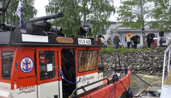 Sjöräddningsbåt snett bakifrån. Folk med paraplyn syns ovanför hamnen