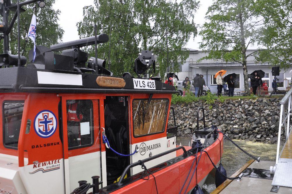 Sjöräddningsbåt snett bakifrån. Folk med paraplyn syns ovanför hamnen