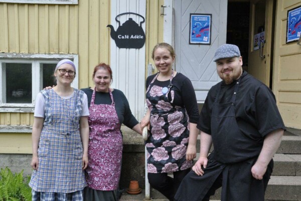 fyra personer utanför ett hus. Caféskylt syns bakom dem