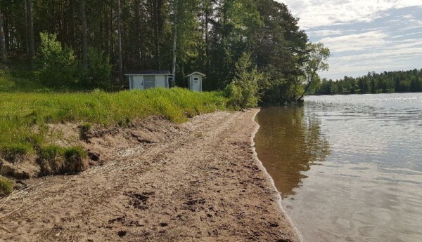 Strandlinje av badstrand. Längre bort syns små träbyggnader för omklädning.