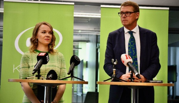 Två personer står vid små bord med mikrofoner