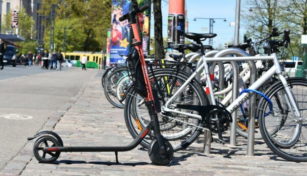 En elsparkcykel står parkerad intill flera cyklar i stadsmiljö.